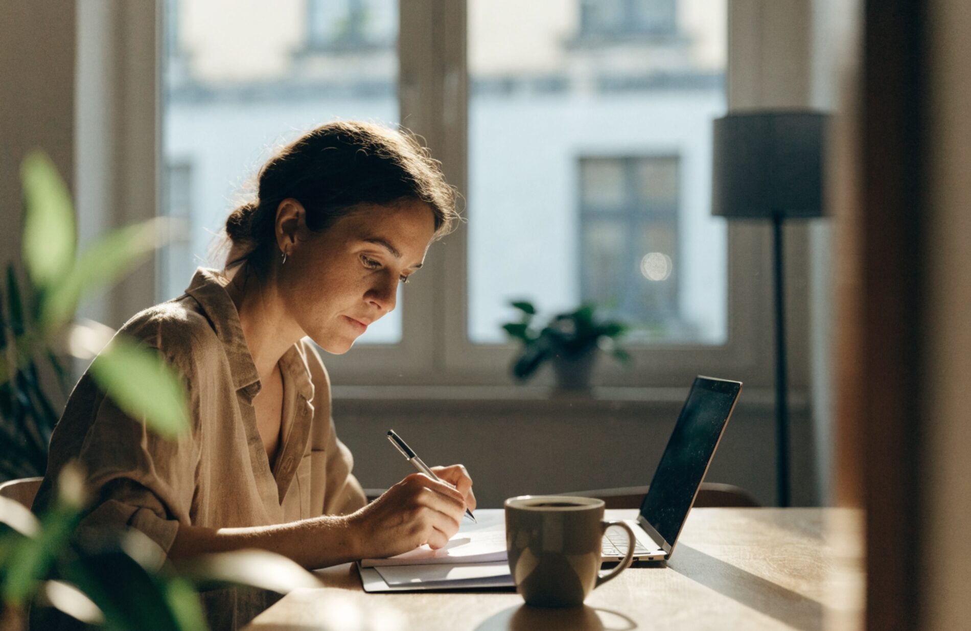 A woman sitting at a sunlit table at home, calmly preparing her immigration paperwork